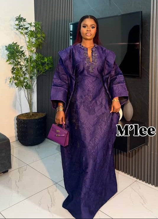 Woman in a purple dress holding a matching handbag indoors.